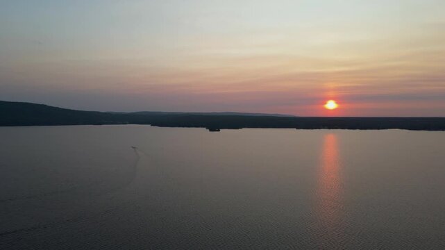Aerial shot of boat driving towards beautiful sunset over lake and forest covered hillside. Calagbogie Ontatio