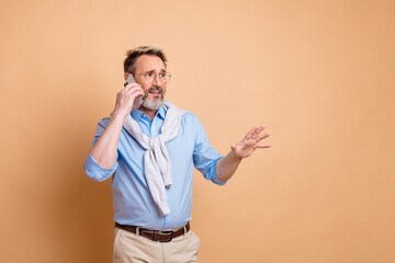 Mature businessman gesturing while on phone with stylish outfit and beige background showing...
