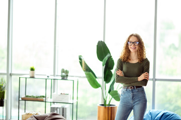 Confident young woman with curly hair in casual attire smiling in a modern interior workspace with plants and natural light