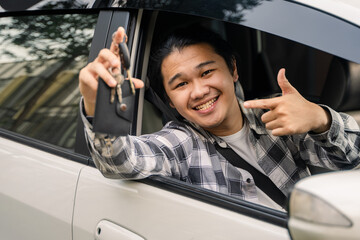Asian man sitting in a white car, smiling confidently while giving a thumbs-up and holding car keys...