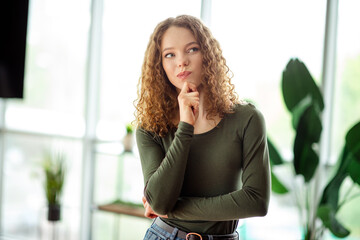 Young woman with thoughtful expression in bright indoor space, wearing casual attire, surrounded by...