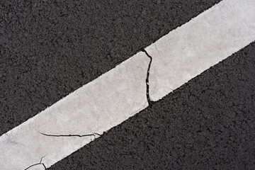 Cracked white diagonal line on a dark asphalt road. Abstract texture of weathered street marking on...