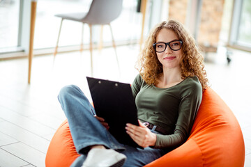 Young woman working comfortably in a modern setting with natural light, sitting relaxed and holding...