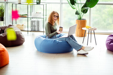 Young woman works on a laptop in a cozy coworking area, enjoying coffee with a relaxed atmosphere...