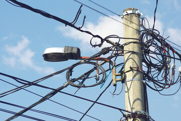 Mess of tangled electric cables on concrete pole with street lamp against blue sky. Concept of...