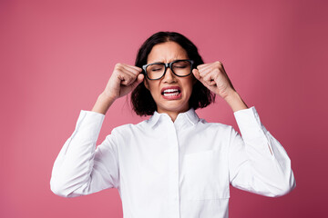Confident young woman in white shirt and glasses expressing emotion on a pink background for...