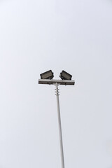 Minimalist shot of a stadium floodlight pole with two lamps against a plain white sky. Modern street lighting equipment with copy space.