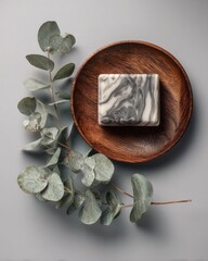 Gray-white soap bar on wooden dish, eucalyptus sprigs