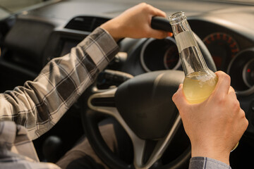 Close-up of an Asian man's hands inside a car, holding the steering wheel with one hand and a clear...