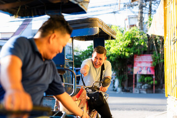 Middle-aged Southeast Asian man pointing angrily at another tricycle driver during a heated...