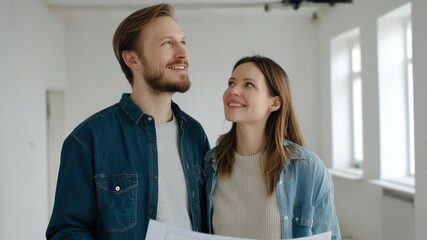 Happy couple holding blueprints in bright, empty room, envisioning future home