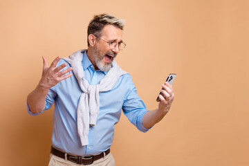 Mature business professional gesturing enthusiastically and talking on smartphone against a beige background