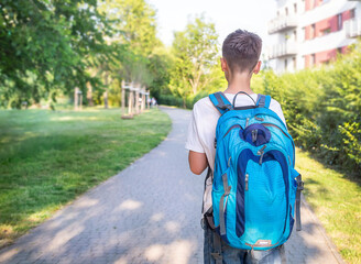 Caucasian boy (schoolboy, kid, pupil, student) with backpack standing on the road to the school. Child ready for new semester (education) in school. Welcome back to school. 
