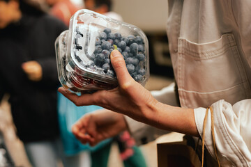 Close-up of hand with fresh berry in plastic packaging at local urban market. Organic produce on sale at outdoor farmer market. Selling fresh crops and veggies harvest. Part of the series © Forewer