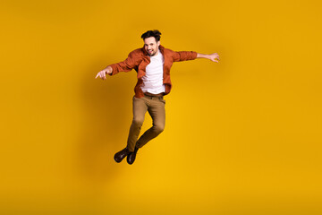 Obraz premium Dynamic portrait of a joyful young man in casual attire jumping energetically on a vibrant yellow backdrop