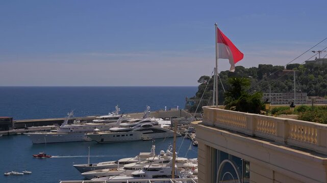 View of luxury yachts docked in Monaco marina under clear blue sky. Monaco flag waving on a sunny day overlooking the Mediterranean Sea in 4K - Monaco 7 May 2019