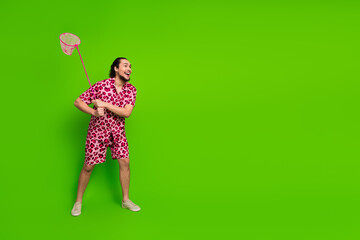 Young man in pink leopard-print outfit holding a pink net, expressing joy against a vibrant green...