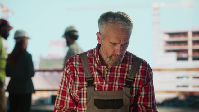 Senior engineer examining blueprints and using tablet on construction site