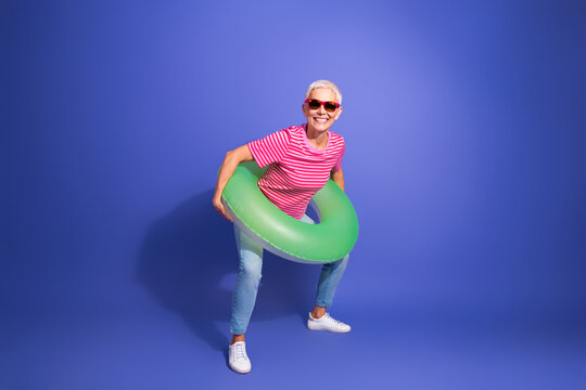 Cheerful elder woman enjoying summer with a green pool float, dressed in casual striped t-shirt against purple