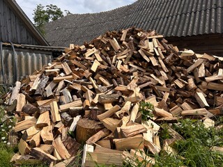 chopped firewood stacked in a pile against the backdrop of a village building
