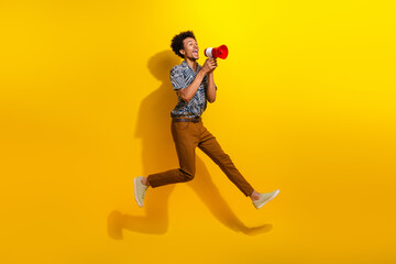 Energetic young man jumping with a megaphone against a vibrant yellow background conveying...