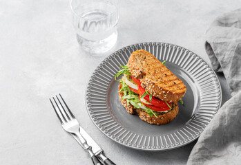 Sandwich of grain bread with fresh tomatoes mozzarella, arugula and pesto on a plate on a light background