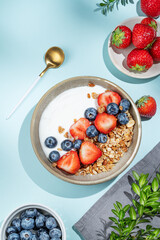 Natural yogurt with granola, blueberry and strawberry in a bowl on a blue  background with spoon