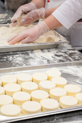 Chefs in uniform prepare cottafe cheese or syrniki on metal trays sprinkled with flour in a bakery...