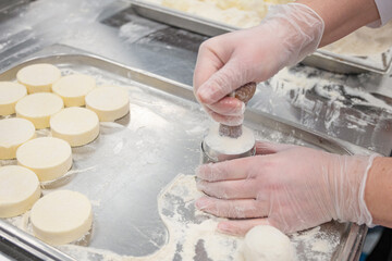 Chef in glooves prepare cottafe cheese or syrniki on metal trays sprinkled with flour in a bakery kitchen.