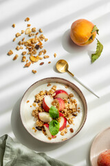 Natural greek yogurt in bowl with peach, mint and scattered granola on white background