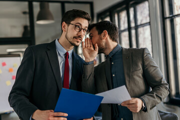 Businessmen whispering and sharing confidential information in office