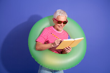 Excited elderly woman with a joyful expression reading and writing in her notebook while wearing a...