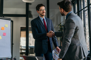 Two smiling businessmen shaking hands after successful meeting in office