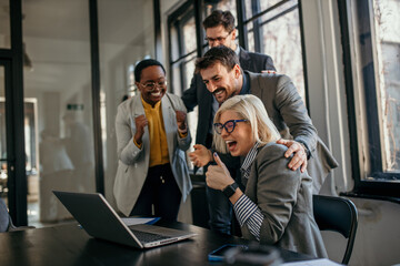 Excited business team celebrating success at work with laptop
