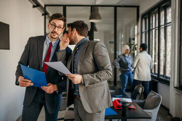 Businessmen whispering and sharing confidential information in office
