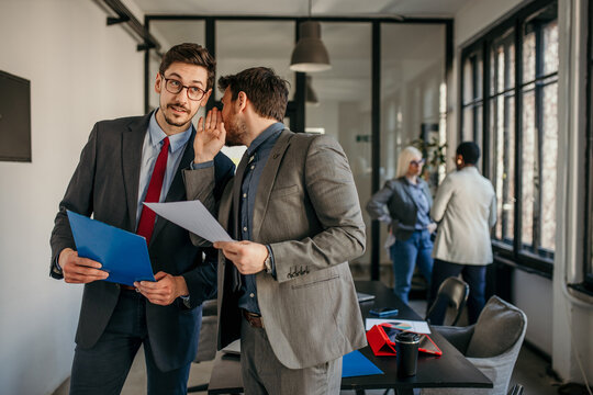 Businessmen whispering and sharing confidential information in office