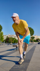 Senior man expressing pain while holding knee during outdoor run. Concept of injury prevention,...