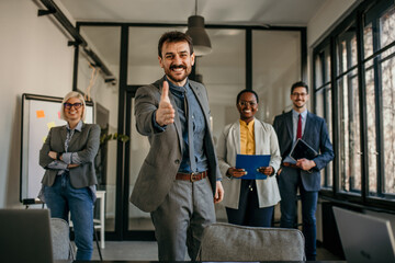 Businessman gesturing thumbs up with multi-ethnic team in modern office