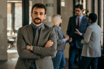 Confident businessman crossing arms while colleagues are talking in background