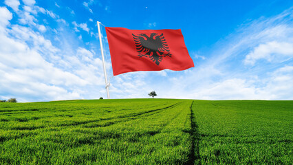 Albania Flag waving on a tall pole over a green field and blue sky
