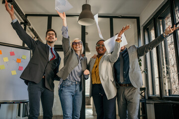 Happy business team throwing papers celebrating success in office
