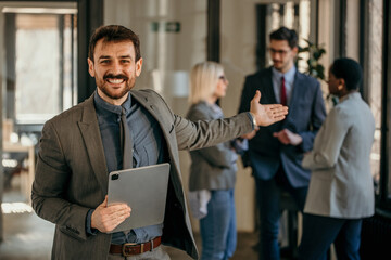 Smiling businessman holding tablet and gesturing to colleagues in office