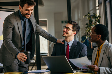 Happy business team celebrating success at meeting with laptop and documents