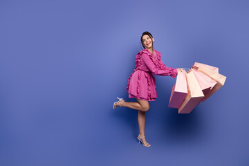 Stylish young woman posing in a vibrant pink dress holding shopping bags against a vivid purple...