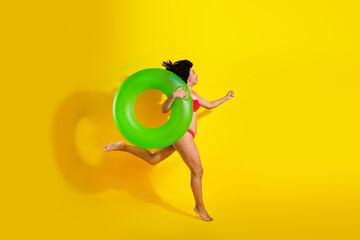 Playful woman in red bikini holding green inflatable ring against bright yellow background, showcasing summer fun