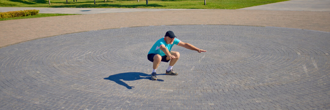 Older man performing deep squat on circular stone pattern in open plaza. Concept of senior fitness, joint health, balance training, mobility workout, strength building. Banner - Powered by Adobe