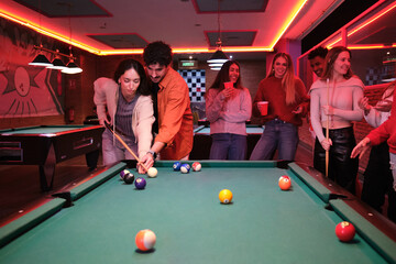 Group of young friends enjoying a game of pool in a billiard hall, socializing and having drinks