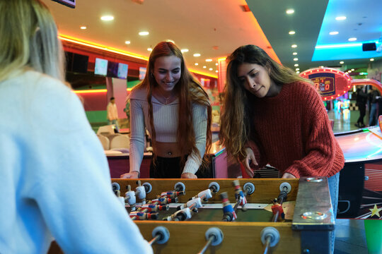 Three young women enjoying a foosball game in a colorful amusement arcade - Powered by Adobe