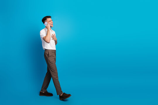 Stylish young man in casual attire talking on smartphone against vibrant blue background representing modern lifestyles