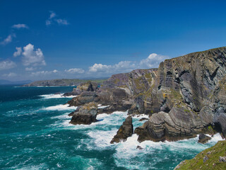 Dramatic cliffs tower over the Atlantic Ocean at Mizen Head, Ireland, under a bright blue sky.